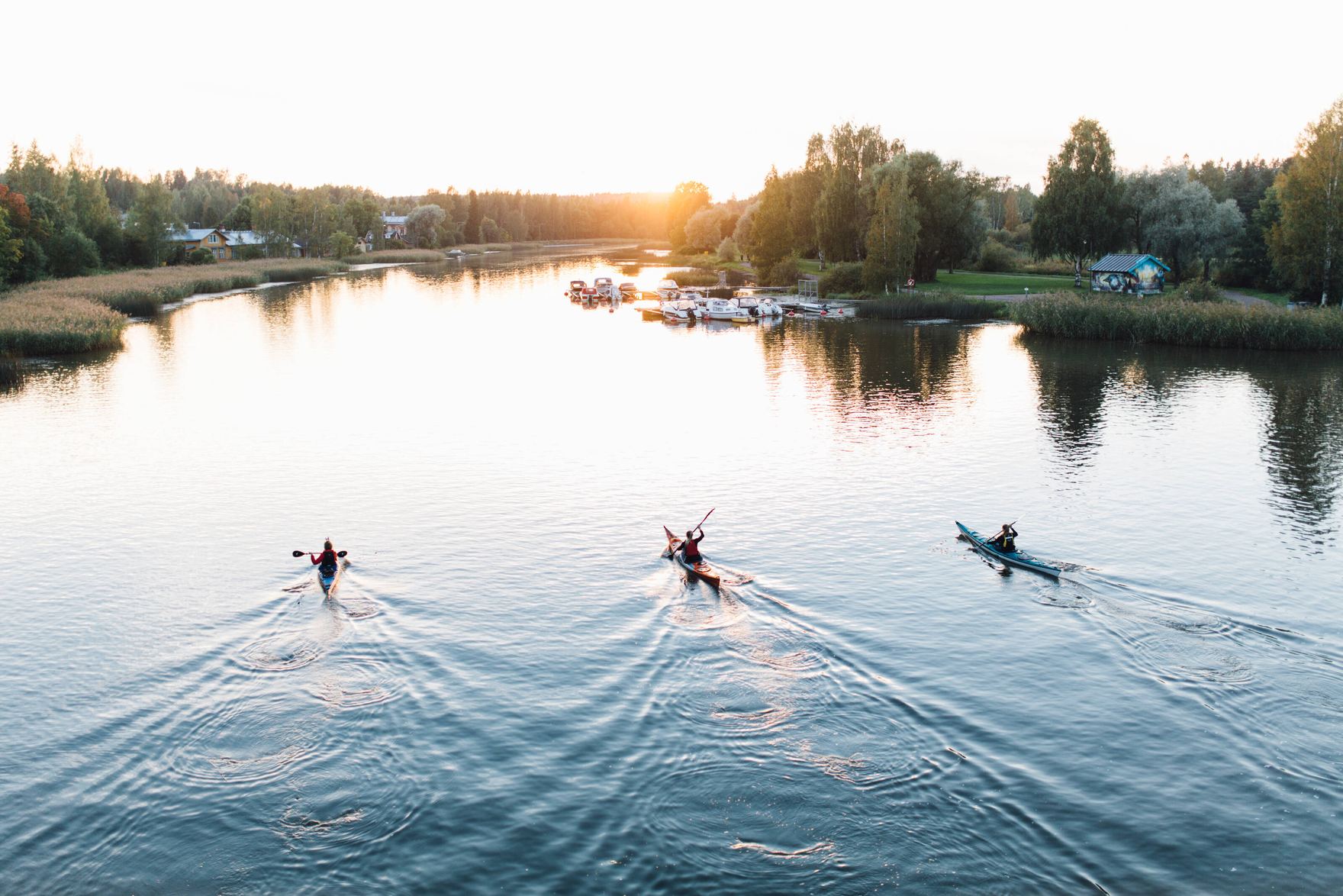 Aerial view of a slender bridge connecting forested islands across a blue Nordic lake.