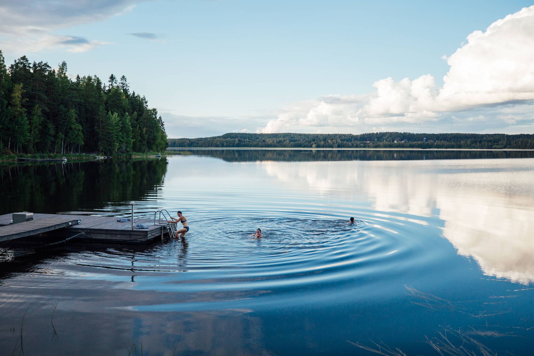 A calm Nordic lake at dusk, forest reflected in still water.